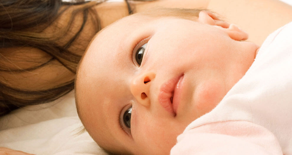 A close-up of a baby's face, partially obscured by a woman's hair.